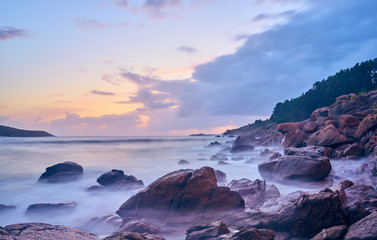 Sunset of the sea with rocks and mountain in the background. Beach and sea water with long exposure.