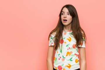 Girl wearing a summer clothes against a red wall being shocked because of something she has seen.