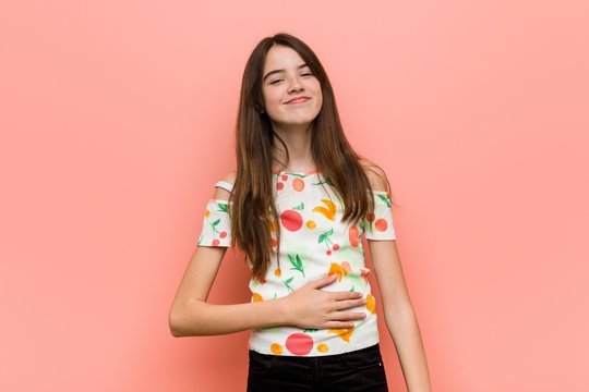 Girl wearing a summer clothes against a red wall touches tummy, smiles gently, eating and satisfaction concept.
