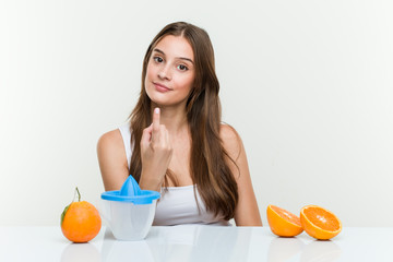 Young caucasian woman with an orange juicer pointing with finger at you as if inviting come closer.