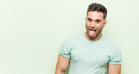 Young handsome man against a green background funny and friendly sticking out tongue.