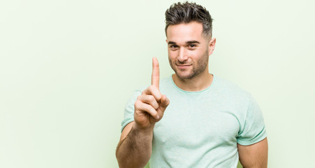 Young handsome man against a green background showing number one with finger.