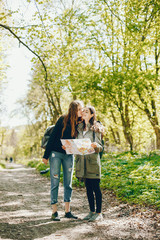 Naklejka premium Two girls standing in a autumn forest. Friends have fun in a park. Tourists use the map.