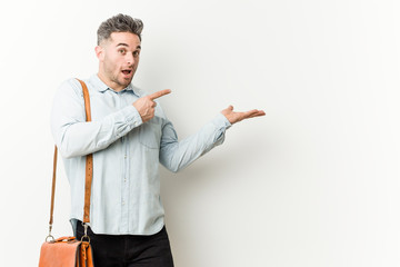 Young handsome business man excited holding a copy space on palm.