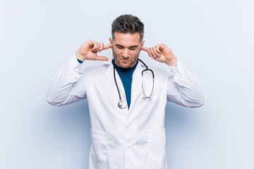 Young handsome doctor man covering ears with hands.