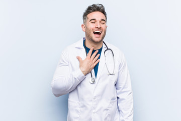 Young handsome doctor man laughs out loudly keeping hand on chest.