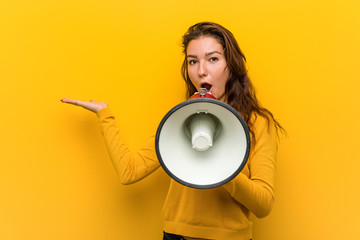Young european woman holding a megaphone impressed holding copy space on palm.
