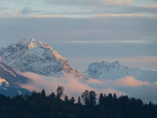 Obraz premium sunset in snowy mountains with low level clouds and black forest silhouette