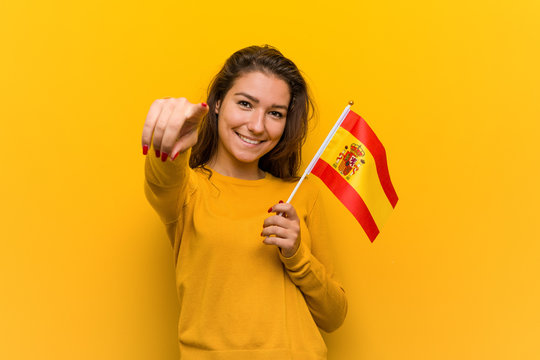Young european woman holding a spanish flag cheerful smiles pointing to front.