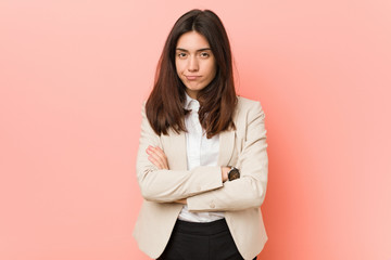 Young brunette business woman against a pink background frowning face in displeasure, keeps arms...