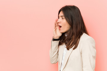 Fototapeta premium Young brunette business woman against a pink background shouting and holding palm near opened mouth.