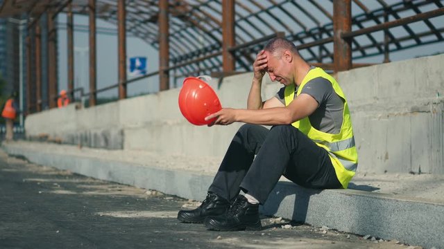 A tired worker at a construction site is upset after hard work and is under stress. Close-up. Worker during a break at the construction of a road on a sunny summer day