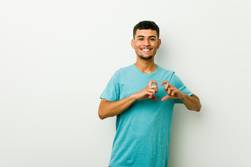 Young hispanic man smiling and showing a heart shape with hands.