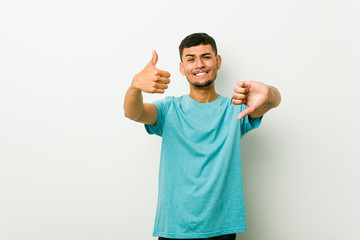 Young hispanic man showing thumbs up and thumbs down, difficult choose concept