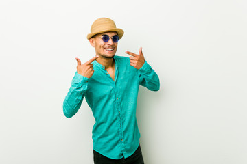 Young hispanic man wearing a summer clothes smiles, pointing fingers at mouth.