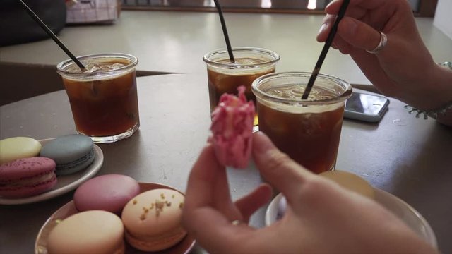 Gourmet girl eats french macaron and drinks iced coffee beverage.