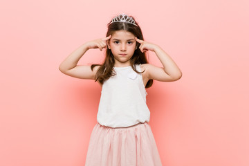 Little girl wearing a princess look focused on a task, keeping forefingers pointing head.