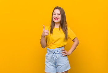 Young woman teenager wearing a yellow shirt smiling and raising thumb up