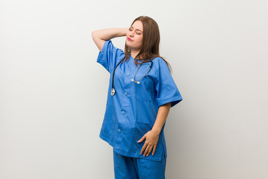 Young Nurse Woman Against A White Wall Touching Back Of Head, Thinking And Making A Choice.