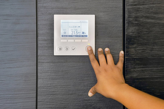 African woman hand try to turn on the new air condition in room, in the hotel room. African  female hands on the air conditioning control panel. Hand girl setting temperature air condition.           