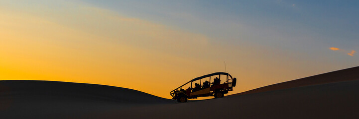 Fototapeta na wymiar Silhouette of a buggy with tourists at sunset in the coastal Peruvian desert between Ica and Huacachina, Peru.
