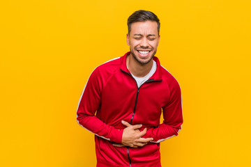Young filipino fitness man laughs happily and has fun keeping hands on stomach.