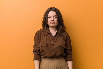 Young curvy russian woman blows cheeks, has tired expression. Facial expression concept.