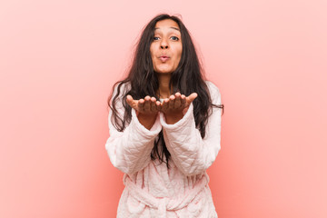 Young indian woman wearing pajama folding lips and holding palms to send air kiss.