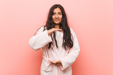 Young indian woman wearing pajama holding something with both hands, product presentation.