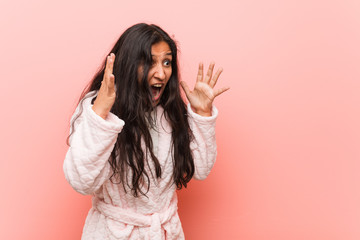 Young indian woman wearing pajama shouts loud, keeps eyes opened and hands tense.