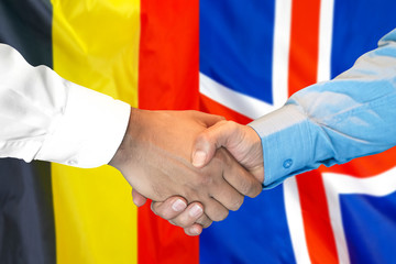 Handshake on Belgium and Iceland flag background.