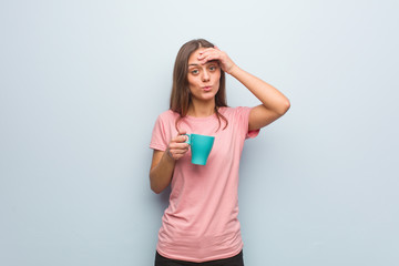 Young pretty caucasian woman worried and overwhelmed. She is holding a mug.