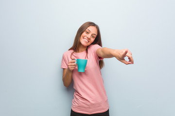 Fototapeta premium Young pretty caucasian woman cheerful and smiling pointing to front. She is holding a mug.