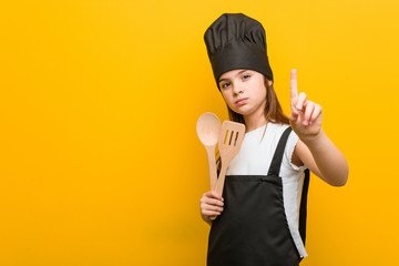 Little caucasian girl wearing a chef costume showing number one with finger.