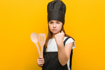 Little caucasian girl wearing a chef costume showing fist to camera, aggressive facial expression.