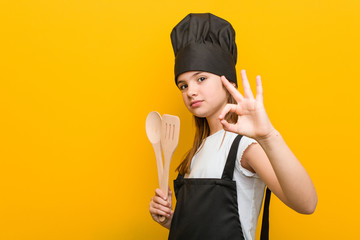 Little caucasian girl wearing a chef costume cheerful and confident showing ok gesture.