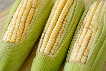 Closeup of raw corn cobs with straw over wood