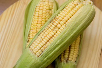 Closeup of raw corn cobs with straw over wood