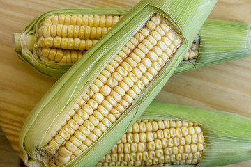 Closeup of raw corn cobs with straw over wood