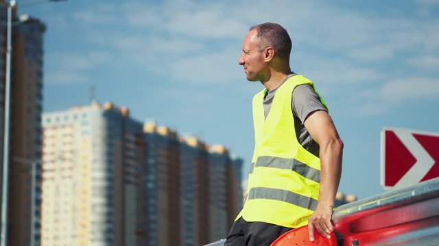 A tired worker at a construction site is upset after hard work and is under stress. Close-up. Worker during a break at the construction of a road on a sunny summer day