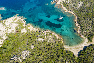 View from above, stunning aerial view of a sailboat floating on a beautiful turquoise sea that bathes the green and rocky coasts of Sardinia. Emerald Coast (Costa Smeralda) Italy