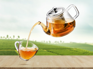 Jug pouring hot tea into glass cup in the air with tea plantations, Healthy products by organic natural ingredients concept, Empty space in studio shot