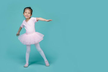 Beautiful smiling Asian little girl in a pink suit is dancing a ballet at school, empty space in...