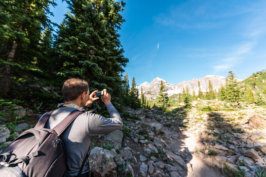 Maroon Bells peak in Aspen, Colorado with tourist man backpack hiker taking picture with camera in July 2019 summer on trail path road wide angle view
