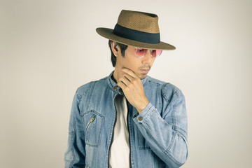 Young Asian Man in Jeans or Denim Jacket Wear Red Glasses and Hat Touching Chin Pose in Vintage Tone
