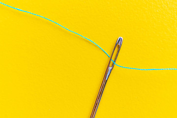 macro shot of a needle eye with a thread going through it on color background