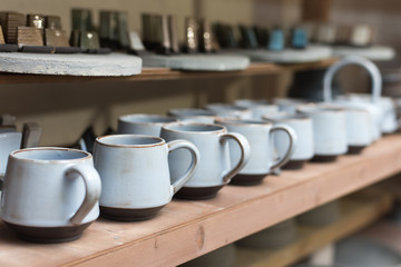 glazed ceramic dishes stand on a shelf in the workshop shelving with handmade ceramic and clay mugs
