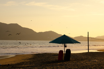 Pacific Ocean sunset with umbrella and surfing boards