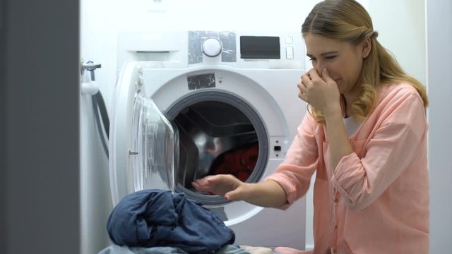Woman closing nose from stinky clothes after washing, low-quality soap-powder