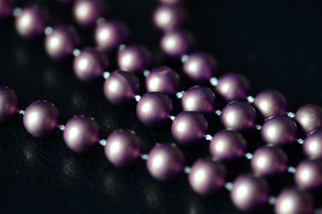 Long beaded necklace purple color on a dark background close up